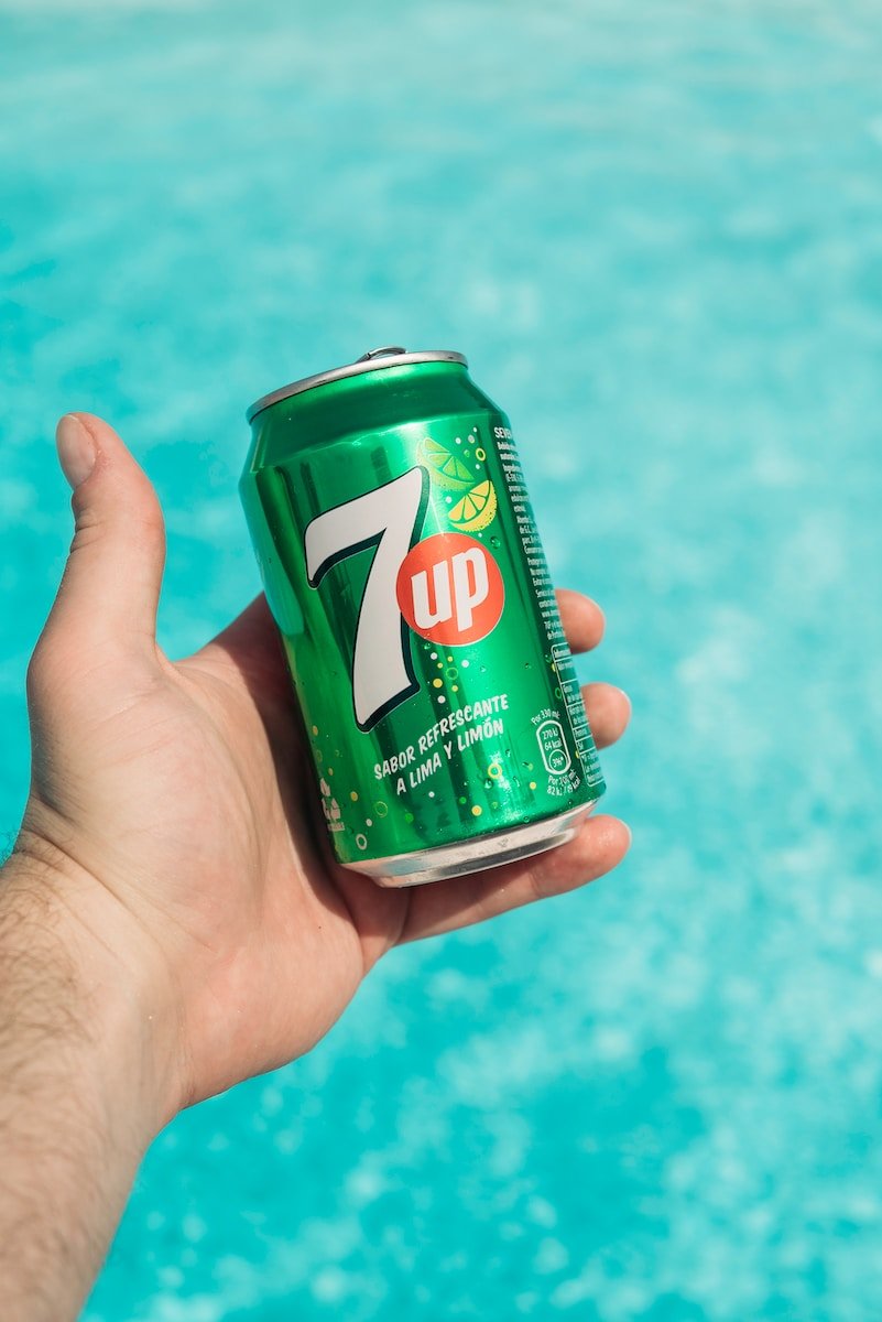 a hand holding a can of 7up by a pool